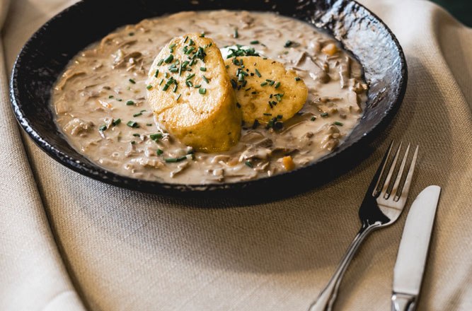 Beuschl with bread dumplings, © Niederösterreich Werbung/David Schreiber A plate with Beuschl and two bread dumplings, garnished with herbs, on a table with cutlery.