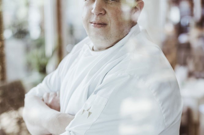 Landlord Christian Widgruber, © Niederösterreich Werbung/David Schreiber A man in chef's clothes stands with his arms folded behind a pane of glass.