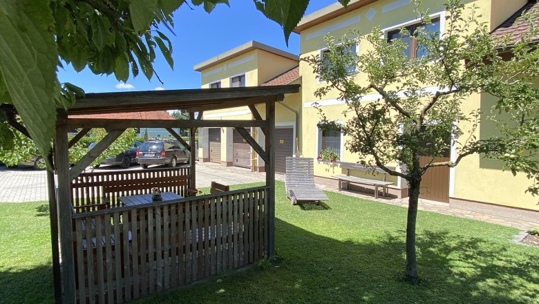 House view, © Privatzimmer Leeb Garden with pavilion, yellow house and car in the background.