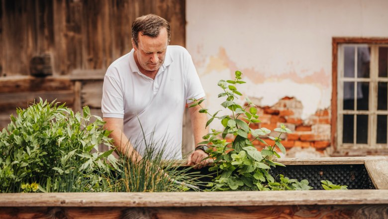Landlord Franz Kloimwieder, © Niederösterreich Werbung/Daniela Führer A man in a white shirt works in a raised bed of herbs in front of an old brick wall.
