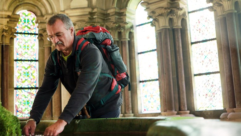 Lilienfeld Abbey, © Mostviertel Tourismus/Weinfranz.at A man with a rucksack bends over a pool of water in a historic building with stained glass windows.