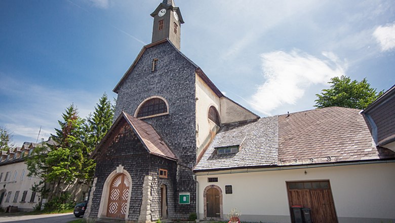 Josefsberg parish church, © Fred Lindmoser Josefsberg parish church with stone-clad façade and tower under a blue sky.