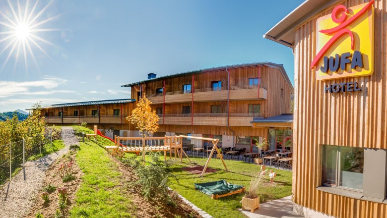 JUFA Hotel Annaberg Mountain Experience Resort, © JUFA Hotels JUFA Hotel Annaberg with playground and sunny sky.