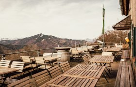 From the terrace, © Stefanie Rysavi Empty terrace with wooden tables and chairs, mountain landscape in the background.