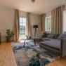 Old post office living room example, © Aumüller Caroline Modern living room with gray sofa, wooden floor and large window with a view of the greenery.