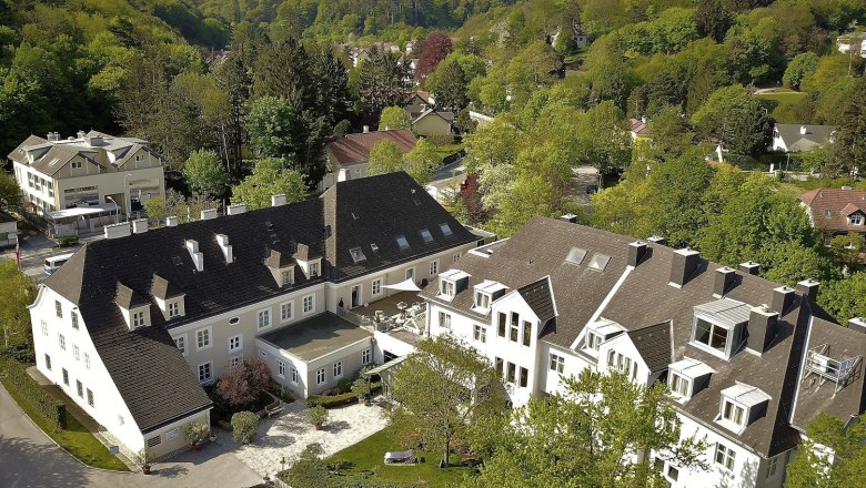 The Hotel Restaurant Höldrichsmühle in a beautiful forest location in Hinterbrühl near Vienna, © Hotel Höldrichsmühle, Jelena Moser Aerial view of a large building complex surrounded by green trees and hills.