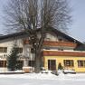 Gasthof Furtner, © Gasthof Furtner An inn in the snow with wooden decorations and a large tree in front of it.