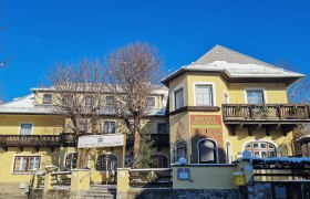 Morning sun - Hotel Kaiser Franz Josef, © Matthias Strutzmann Yellow hotel building with wooden decorations and blue sky in the background.