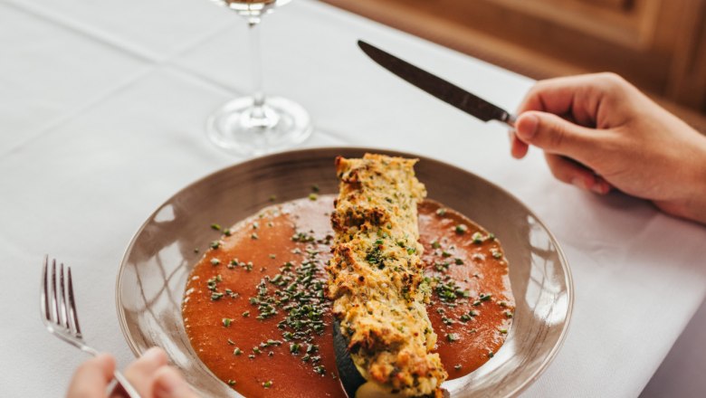 Stuffed zucchinis with tomato sauce, © Niederösterreich Werbung/Daniela Führer Stuffed zucchinis with tomato sauce on a plate, with a glass of white wine next to it.