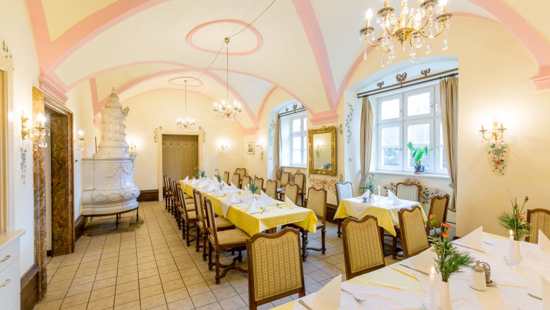 Heiligenkreuz Monastery Inn, © Hammerle Elegant dining room with laid tables, chandeliers and tiled stove.