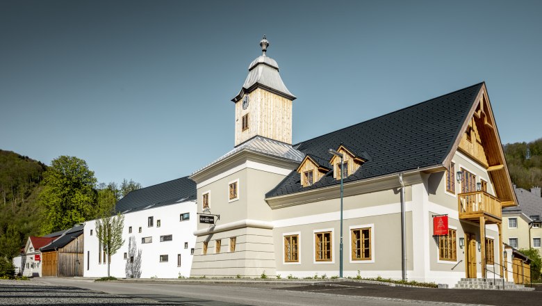 Hotel zum Glockenturm, © croce&wir A modern building with a bell tower and wooden cladding, surrounded by trees and a clear sky.