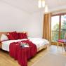Room, © Brandtner Bright bedroom with double bed, red pillows and blanket, wooden floor and large window with curtains.