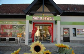 Near & Fresh, © Nah & Frisch Mitterbach Entrance to a Nah & Frisch supermarket with sunflowers in the foreground.