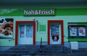 Entrance of a Nah&Frisch store with advertising posters and shop window.