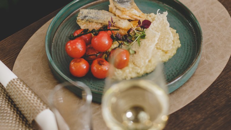 A plate of grilled fish fillet, lemon risotto and cherry tomatoes, with a glass of white wine next to it.
