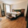 Modern furnished hotel room with double bed, wooden floor and large windows.