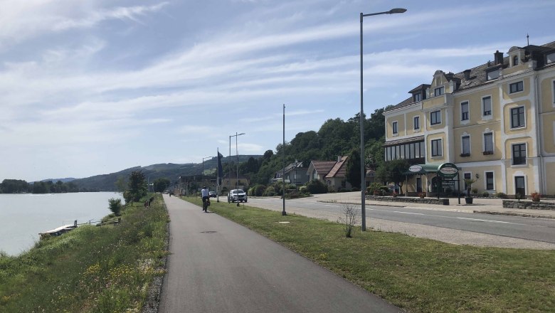 Street on the riverbank with yellow building and cyclist.