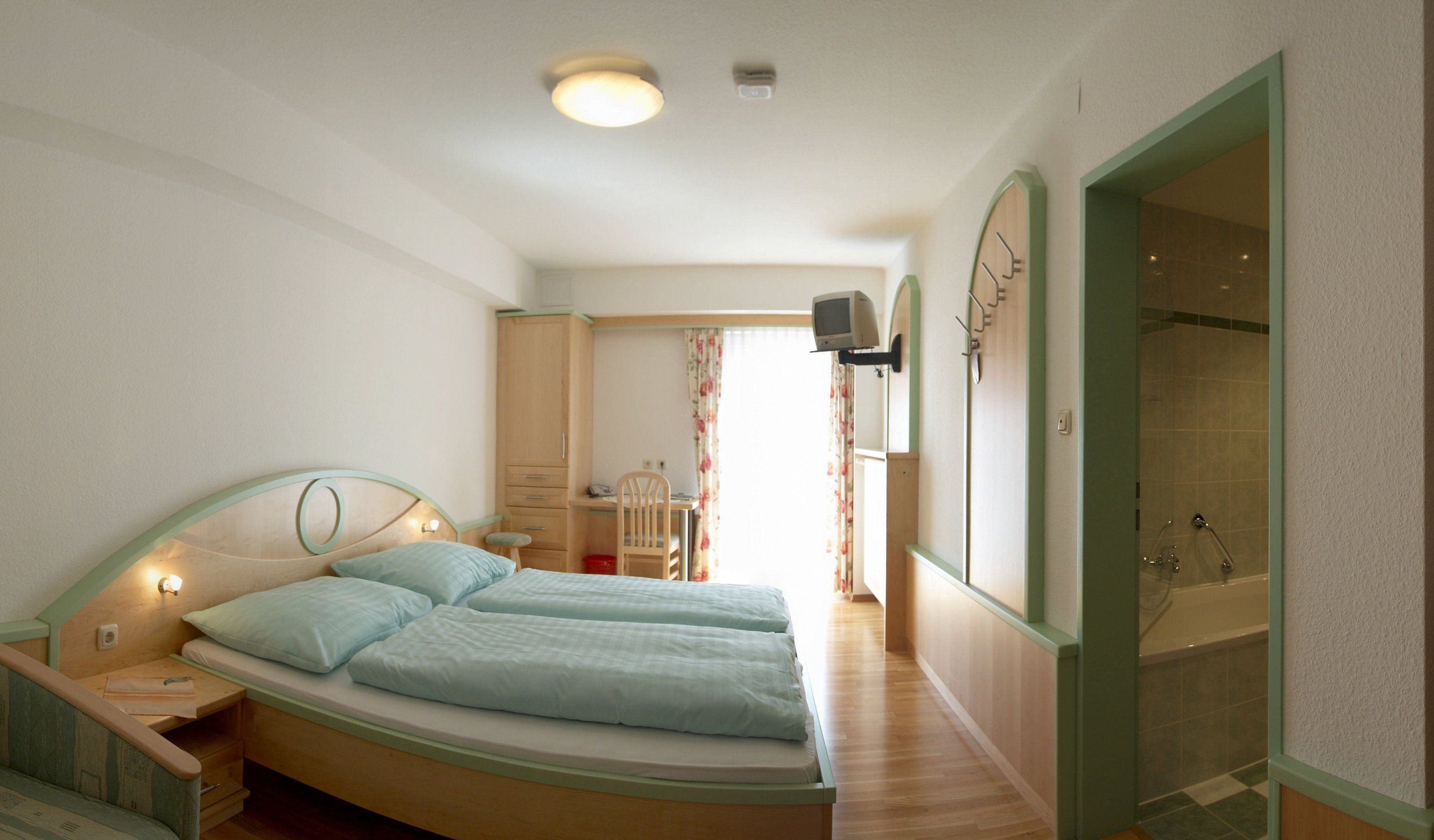 A hotel room with double bed, desk, TV and bathroom.