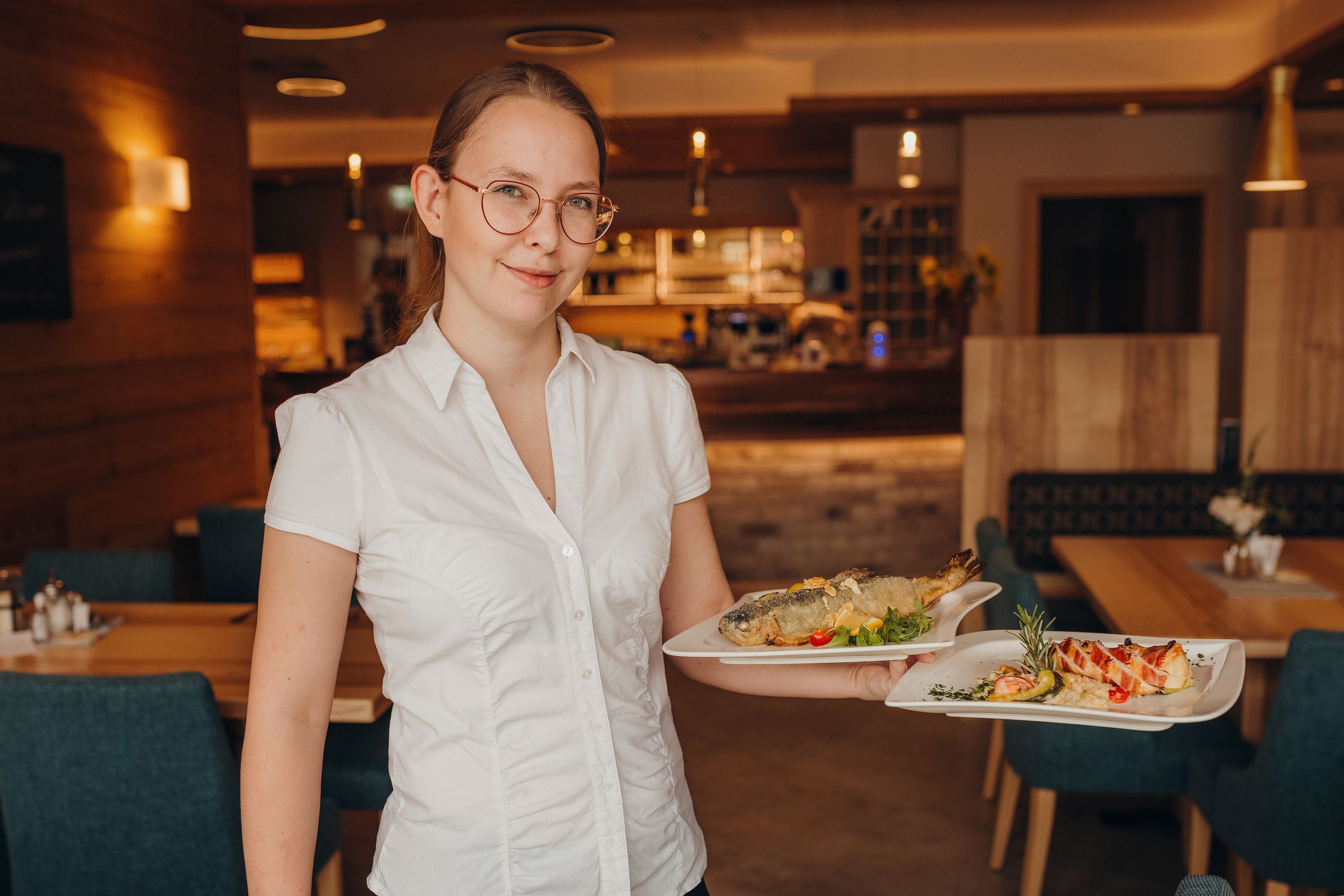 A woman in a restaurant carries two plates of food.