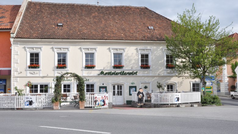 Traditional inn with a white façade and red roof tiles, surrounded by a white fence and flower boxes at the windows.