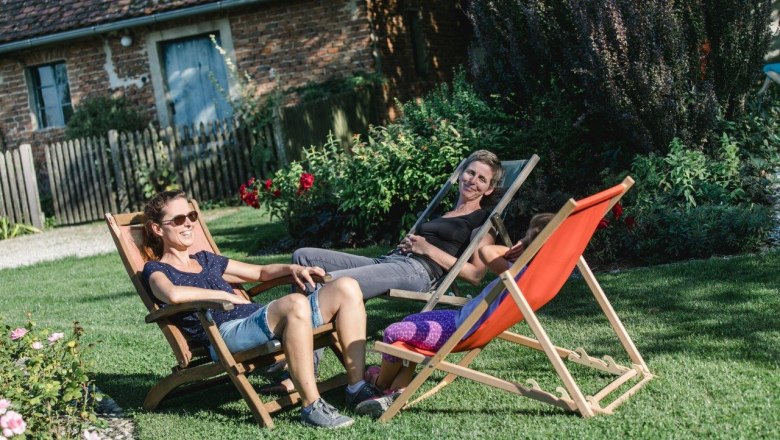 Three people relax on sun loungers in the garden.