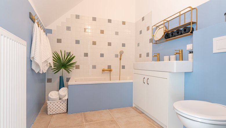 Modern bathroom with blue walls, bathtub, washbasin and golden fittings.