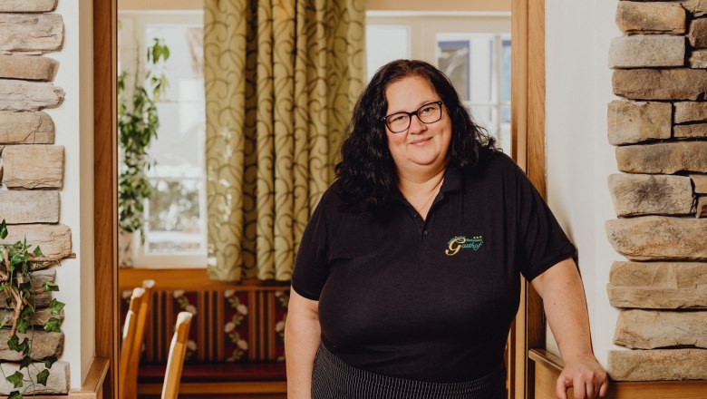 A woman with glasses stands in a cozy inn with stone walls and curtains.