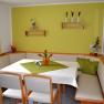 Cozy seating area with corner bench and table in a breakfast room, decorated with green accents and flowers.
