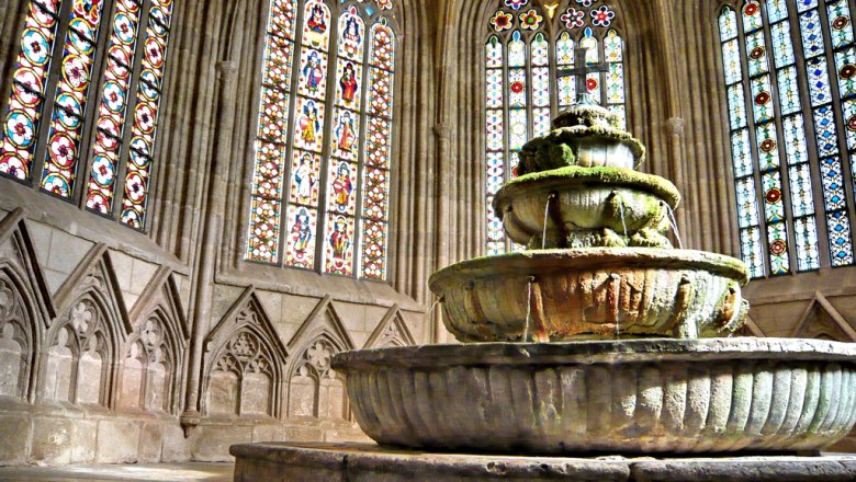 An old fountain in a Gothic building with stained glass windows.
