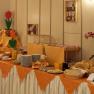 A rich breakfast buffet with bread, rolls, spreads and drinks on a table with an orange cloth.