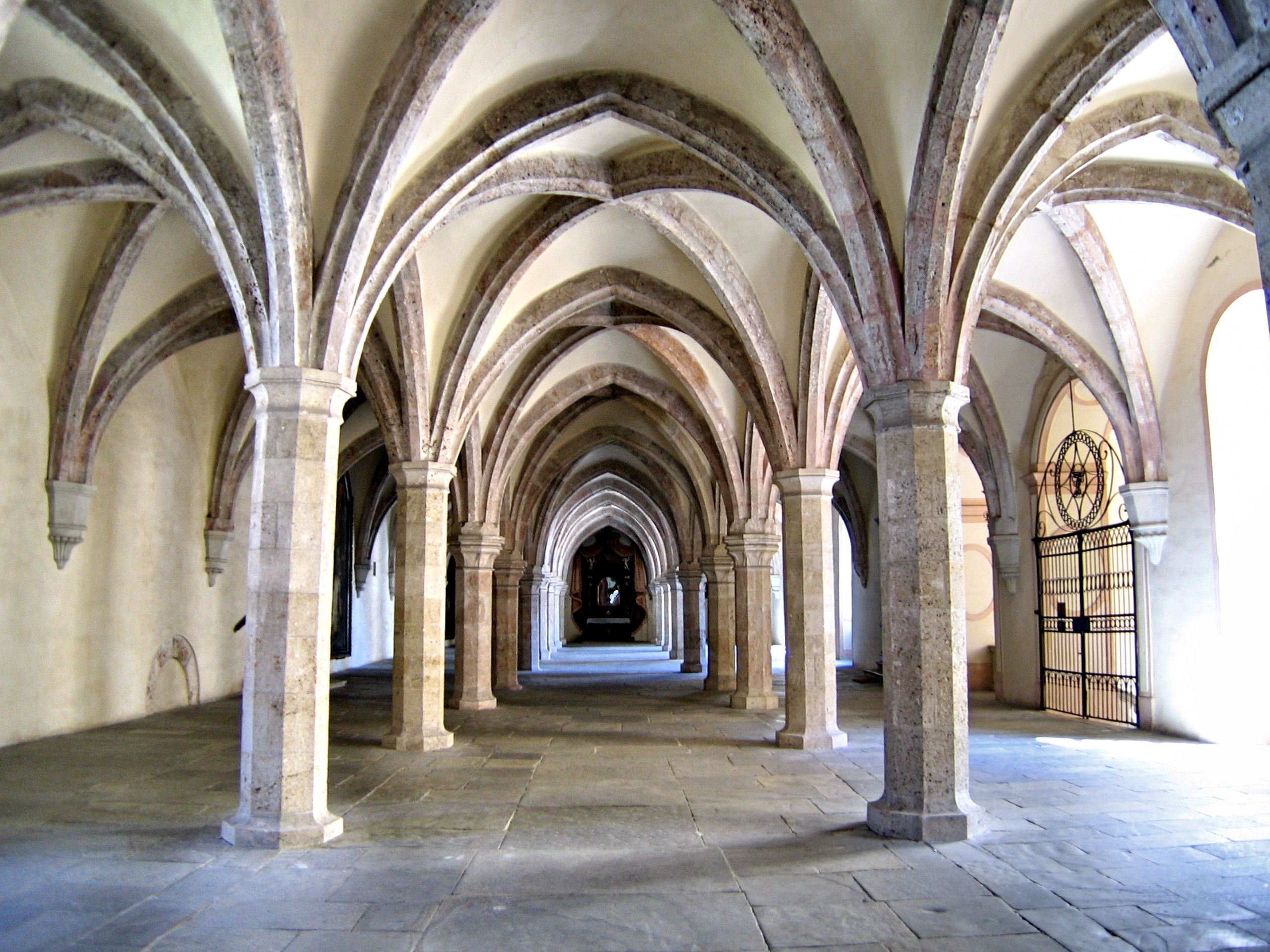 A medieval cloister with Gothic vaults and stone columns.