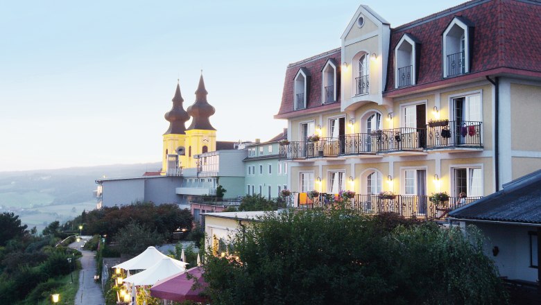 A hotel with balconies and a church in the background at dusk.