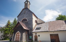 Josefsberg parish church with stone-clad fa&ccedil;ade and tower under a blue sky.