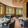 Elegant restaurant with wooden elements, laid tables and large windows overlooking the greenery.