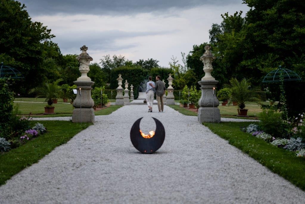 A gravel path in the historic courtyard garden of Seitenstetten Abbey with sculptures and plants, a fireplace in the foreground.