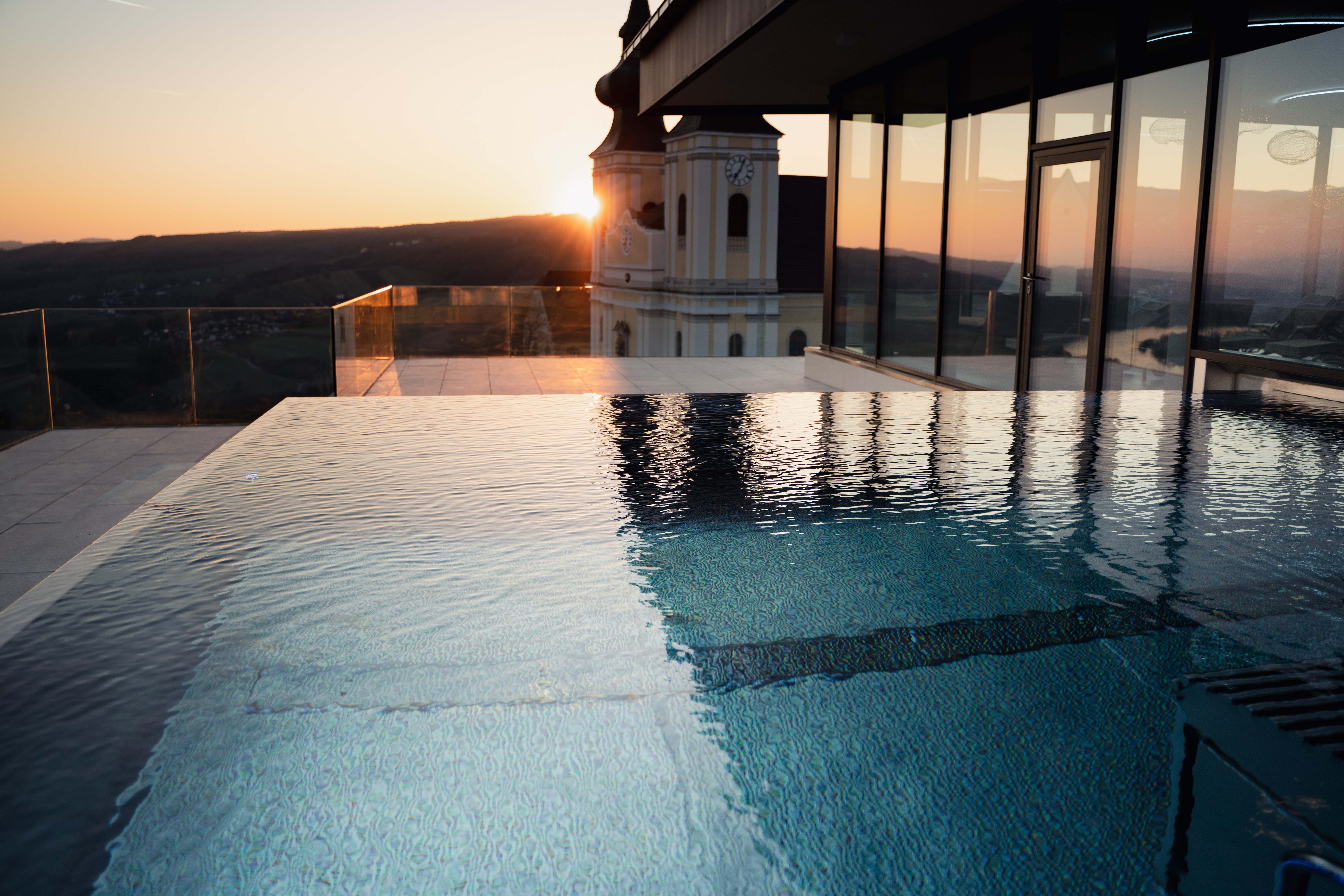Infinity pool at sunset with a view of a building and the landscape.