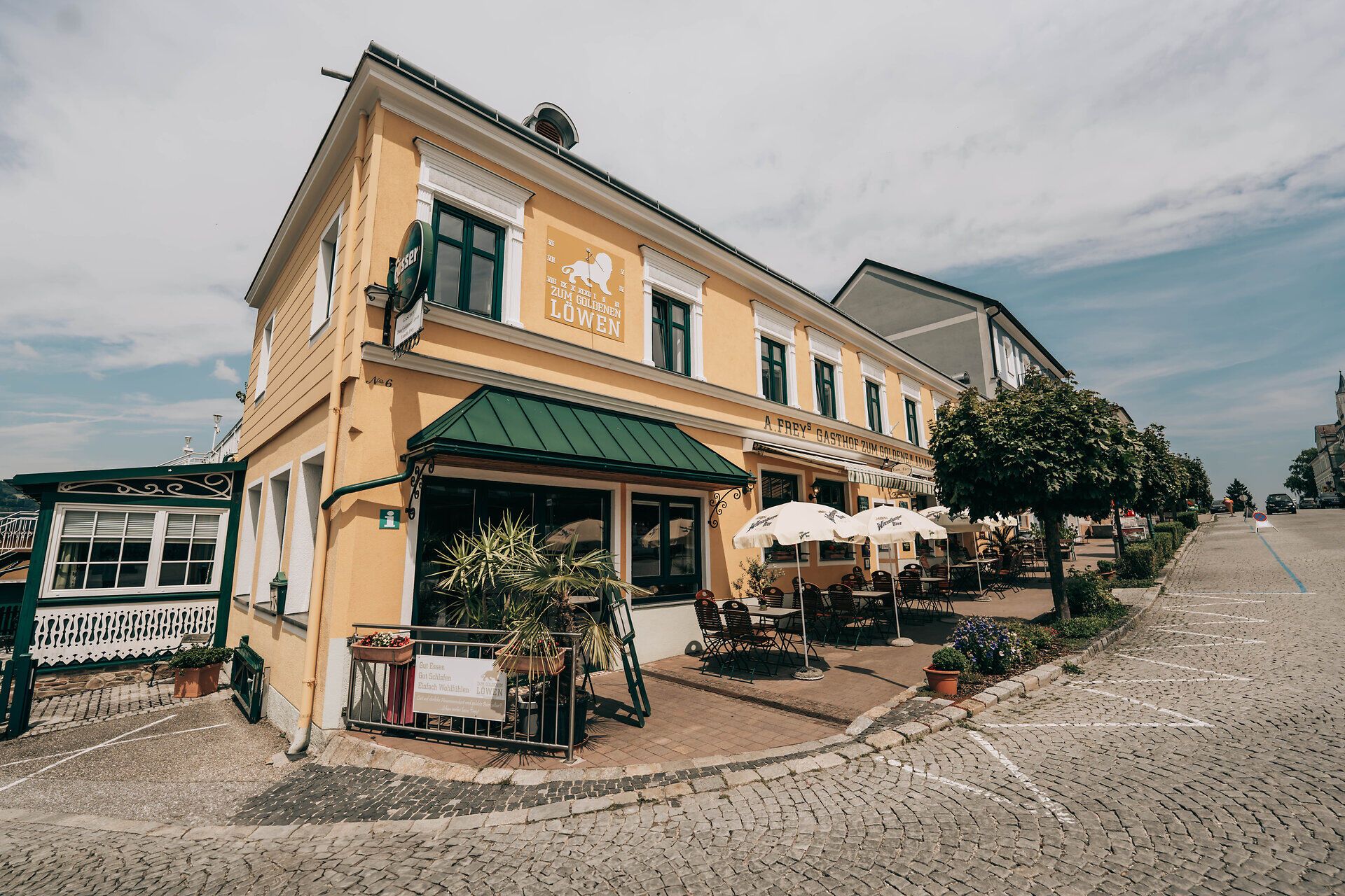 Exterior view of a yellow inn with terrace and parasols.