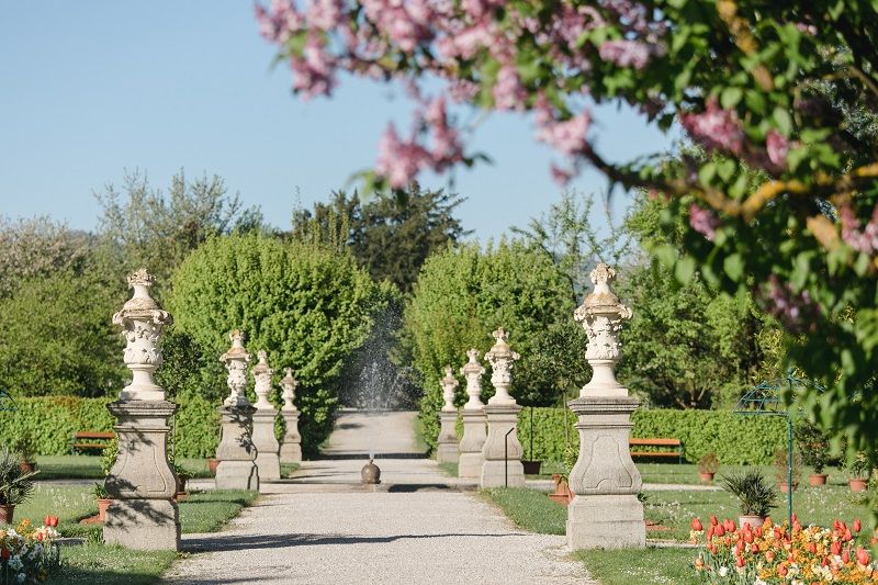 A well-kept garden path with statues and blossoming trees in spring.