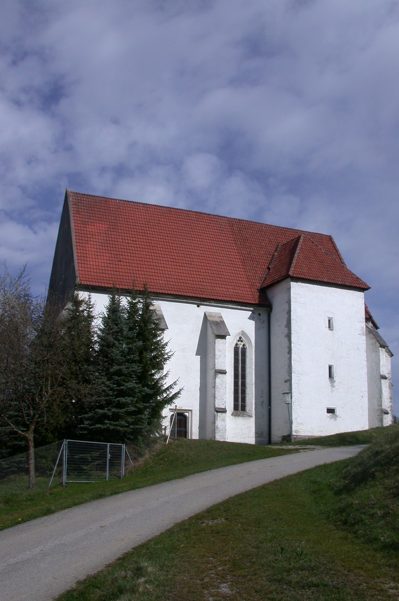 St. Andrew's Church in Kirchberg an der Pielach with a red tiled roof and white façade, surrounded by trees and a path in the foreground.