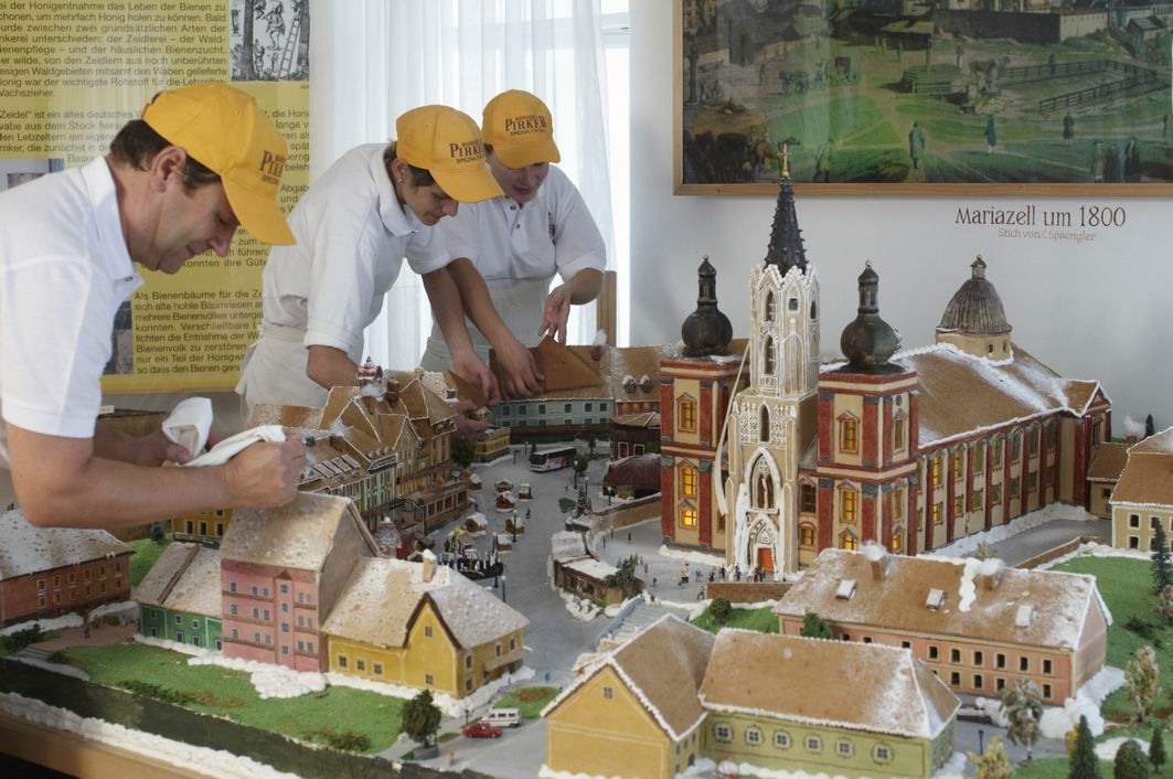 Three people decorate a gingerbread model of Mariazell around 1800.