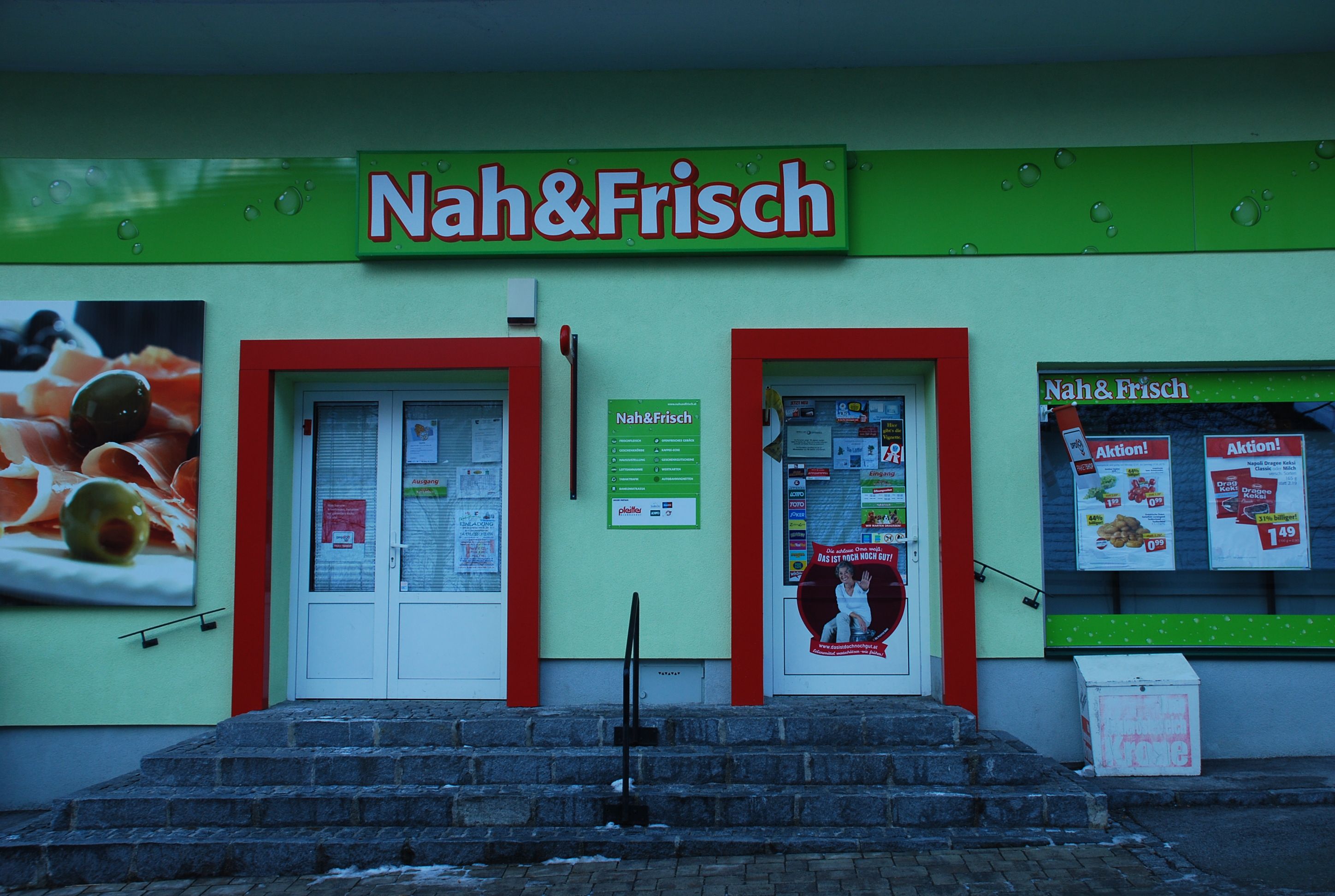 Entrance of a Nah&Frisch store with advertising posters and shop window.