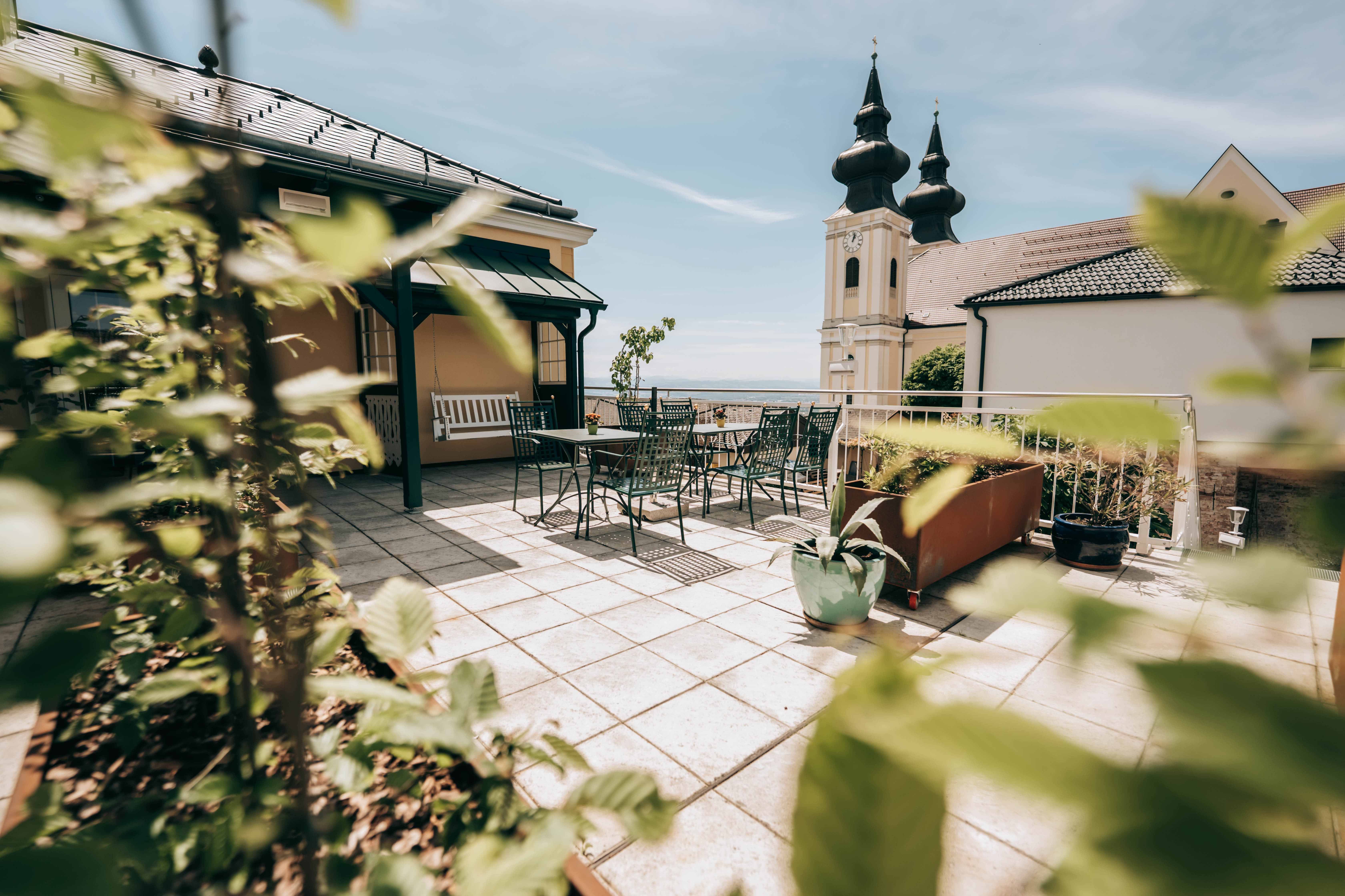 Terrace with table and chairs, church tower with two spires in the background.