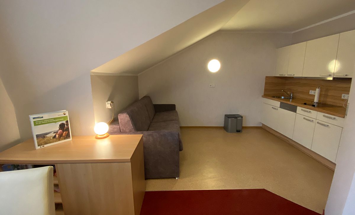 Interior view of a vacation apartment with sofa, table lamp and kitchenette.