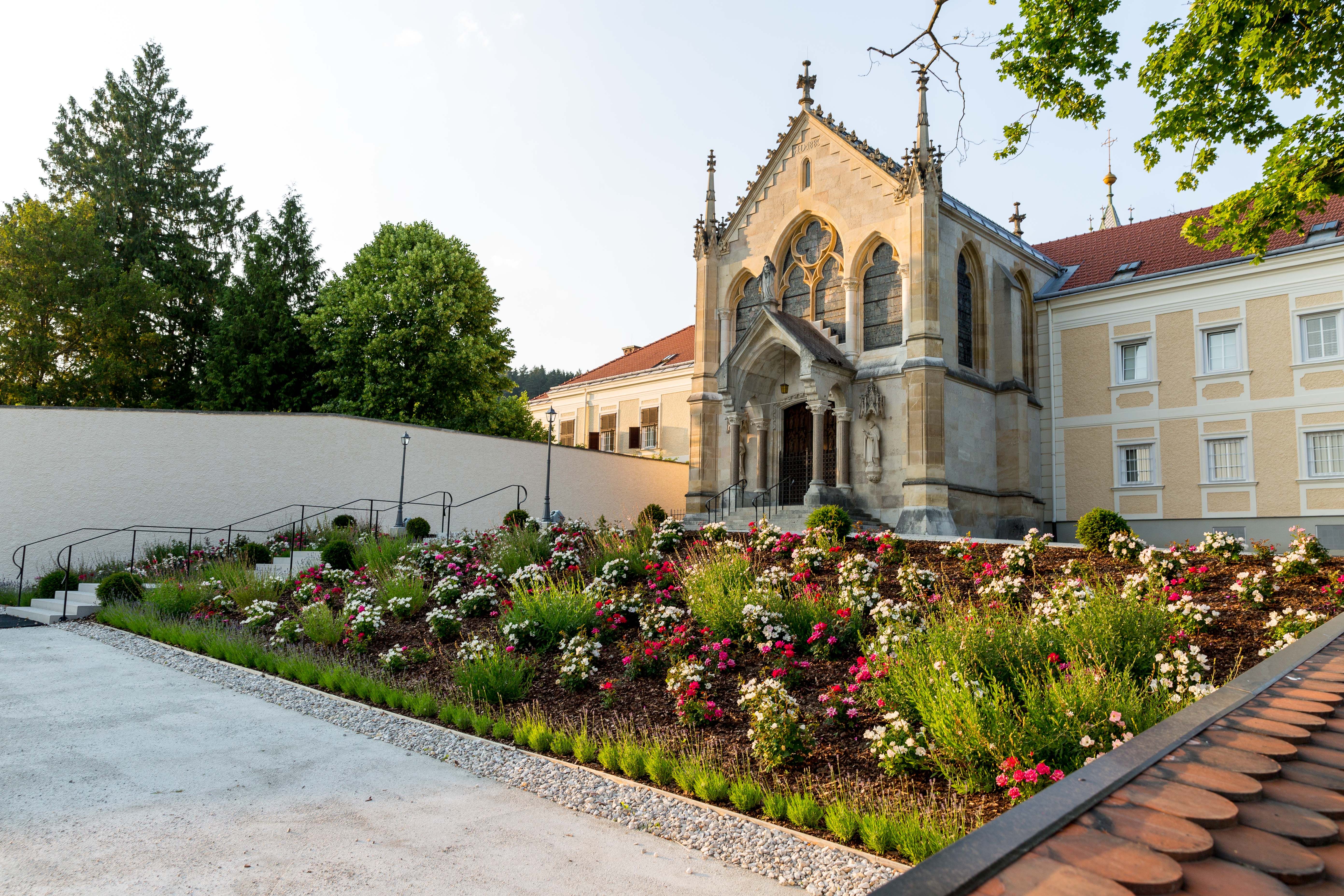 A church with Gothic elements and a well-tended garden full of flowers in the foreground.
