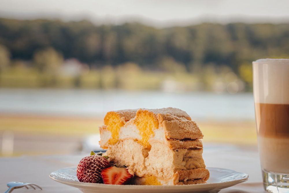 Piece of cake with strawberries and latte macchiato by the lakeside.