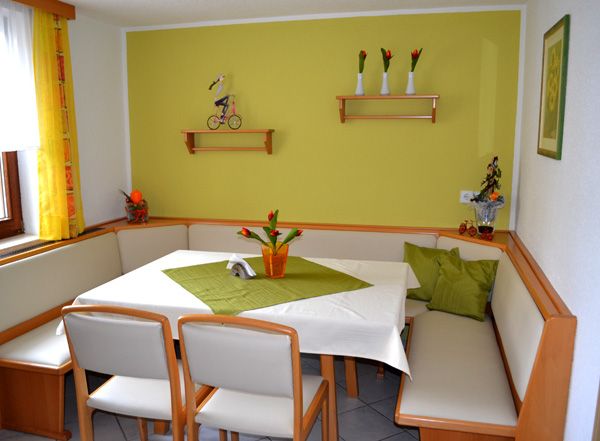 Cozy seating area with corner bench and table in a breakfast room, decorated with green accents and flowers.