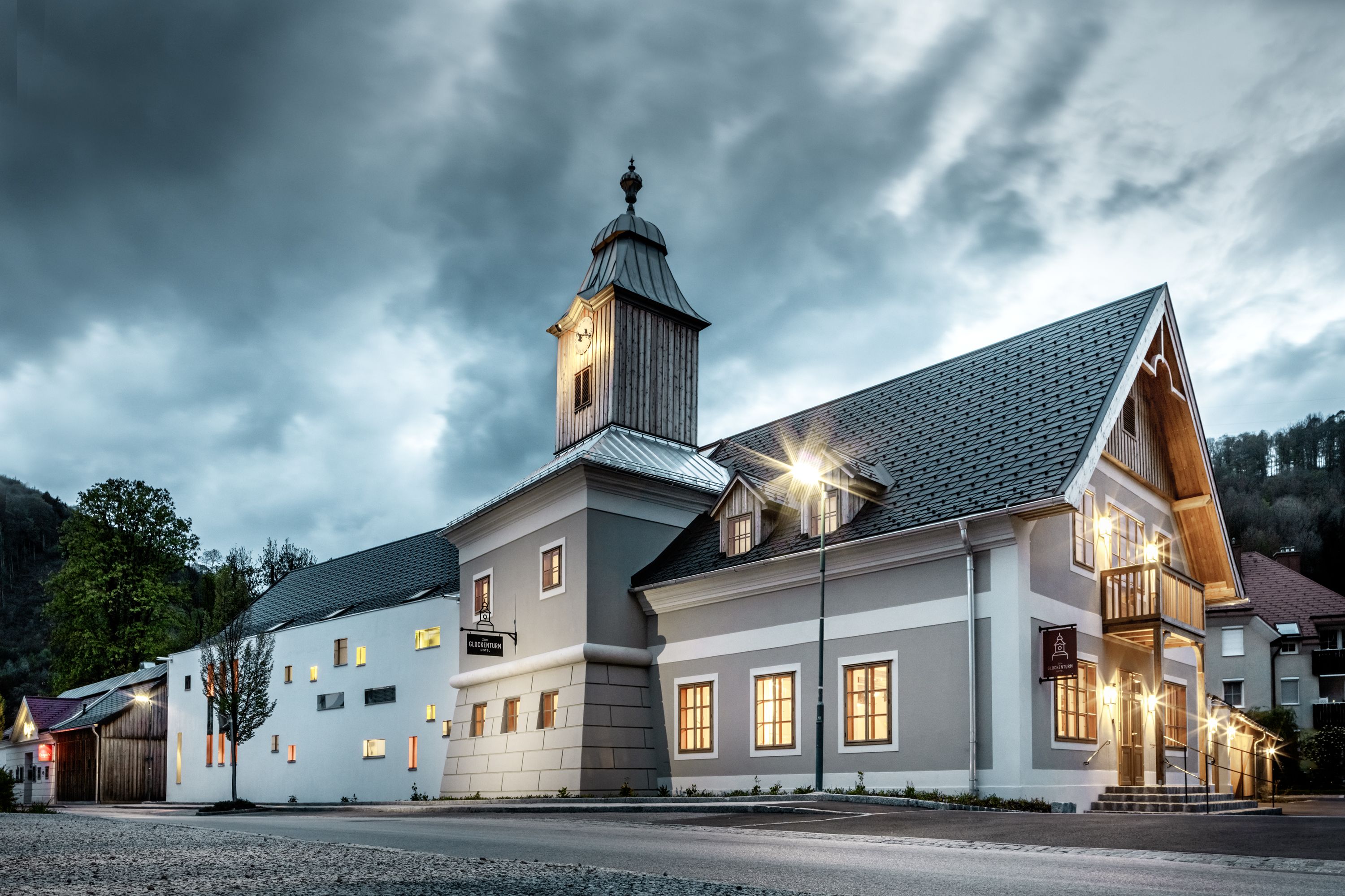 A hotel with a bell tower under a cloudy sky, illuminated by streetlights.