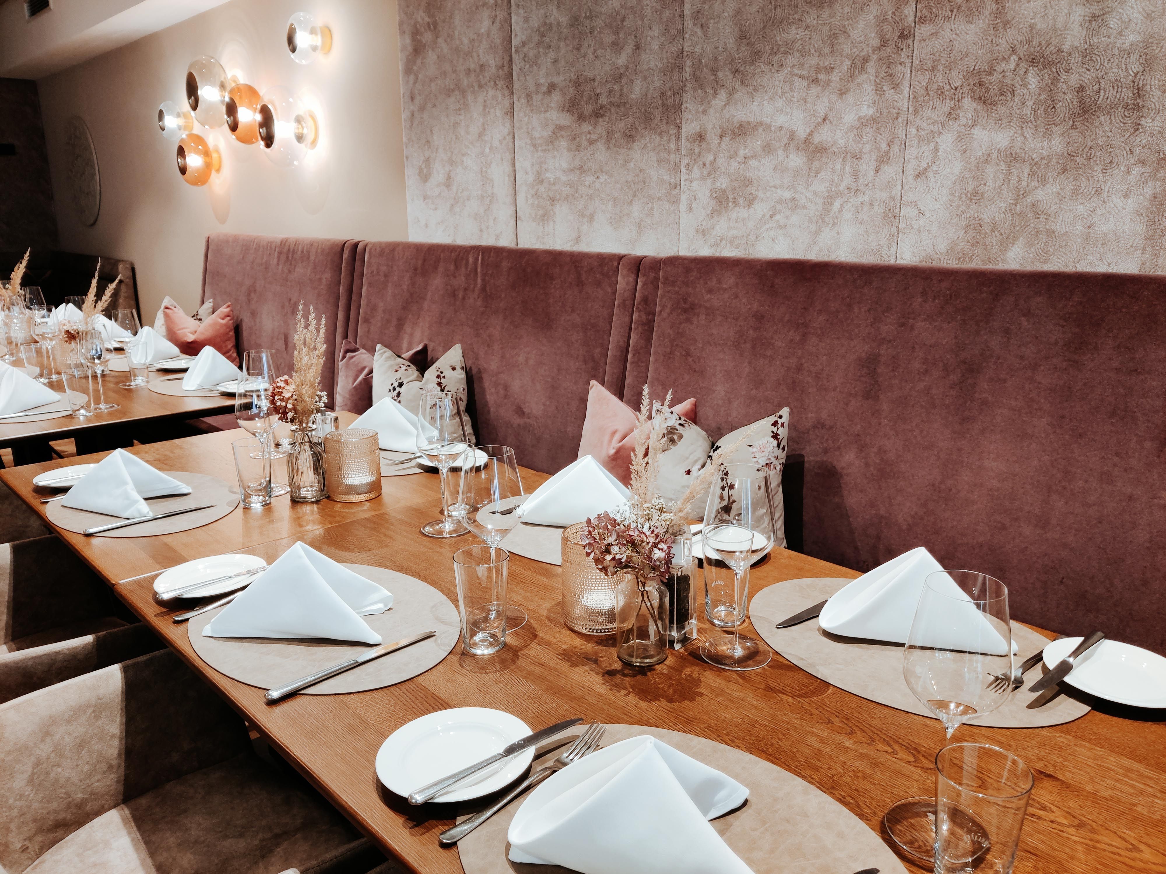 An elegantly laid table in a restaurant with white napkins, glasses and cutlery on a wooden surface.
