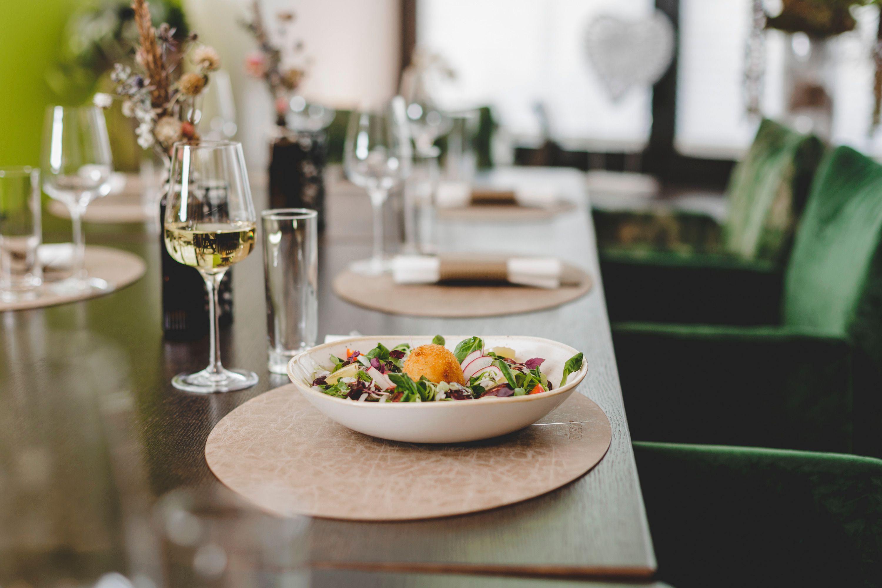 A laid table with a plate of salad and a glass of white wine.