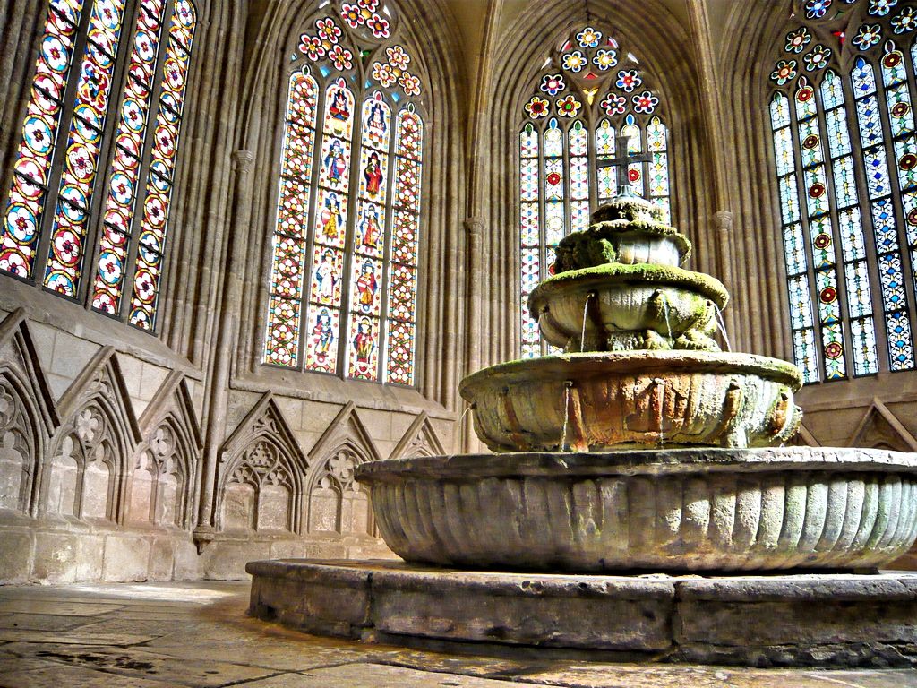 An old fountain in a Gothic building with stained glass windows.